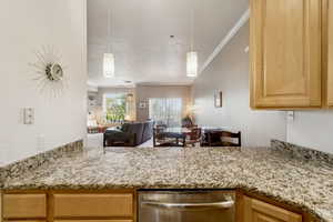Kitchen featuring crown molding, stainless steel dishwasher, light stone countertops, light brown cabinets, and open floor plan