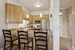 Kitchen featuring stainless steel appliances, light brown cabinets, light stone countertops, a peninsula, and a breakfast bar area