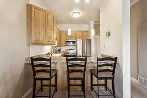 Kitchen with stainless steel appliances, a peninsula, crown molding, light brown cabinetry, and light stone countertops