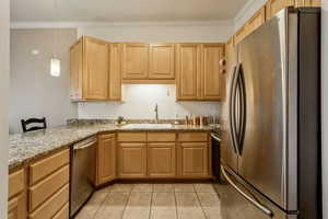 Kitchen with appliances with stainless steel finishes, light tile patterned floors, light stone countertops, ornamental molding, and hanging light fixtures