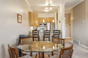 Dining area featuring light carpet, crown molding, and ornate columns