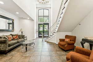 Living room featuring a towering ceiling, stairs, a chandelier, tile patterned floors, and crown molding