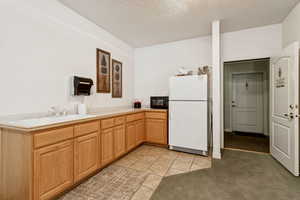 Kitchen with freestanding refrigerator, black microwave, light tile patterned floors, a textured ceiling, and light countertops