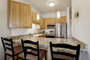 Kitchen with appliances with stainless steel finishes, a peninsula, light stone counters, hanging light fixtures, and crown molding