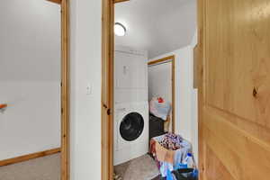 Washroom featuring stacked washer / dryer, carpet flooring, and a textured ceiling