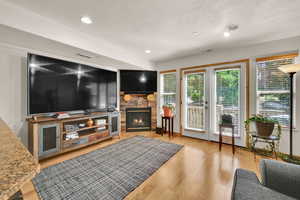 Living area with a fireplace, a textured ceiling, french doors, light wood finished floors, and recessed lighting