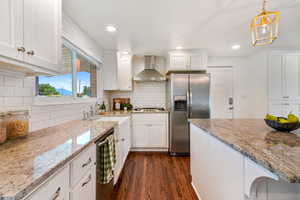 Kitchen featuring wall chimney range hood, stainless steel appliances, dark wood-style floors, white cabinets, and decorative backsplash