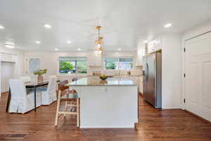 Kitchen featuring stainless steel fridge, white cabinets, light stone countertops, a center island, and tasteful backsplash