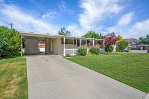 Single story home featuring a porch, driveway, a front yard, brick siding, and a carport