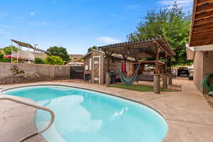 View of swimming pool featuring a pergola, a fenced backyard, a patio, and a shed