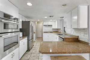 Kitchen featuring appliances with stainless steel finishes, a peninsula, light tile patterned flooring, white cabinetry, and tasteful backsplash