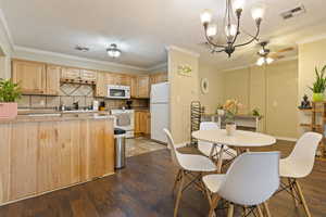 Kitchen featuring white appliances, light brown cabinets, a ceiling fan, dark wood-type flooring, and ornamental molding