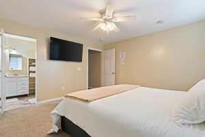 Bedroom with light colored carpet, ceiling fan, and connected bathroom
