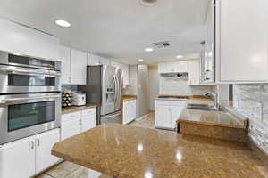 Kitchen with appliances with stainless steel finishes, decorative backsplash, white cabinetry, a peninsula, and recessed lighting
