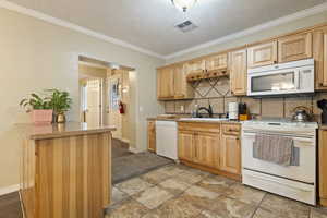 Kitchen with white appliances, decorative backsplash, crown molding, and light countertops