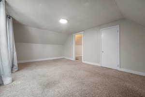 Additional living space featuring vaulted ceiling, carpet flooring, and a textured ceiling