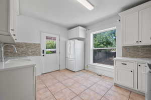 Kitchen with freestanding refrigerator, light tile patterned floors, decorative backsplash, and white cabinets