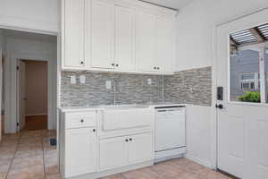 Kitchen with white dishwasher, light countertops, light tile patterned flooring, decorative backsplash, and white cabinets
