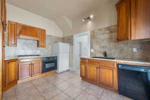 Kitchen with black appliances, premium range hood, brown cabinets, and vaulted ceiling