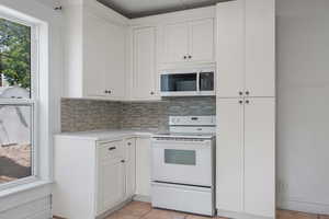 Kitchen with electric range, light countertops, tasteful backsplash, and white cabinets
