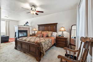 Bedroom with light carpet, a tiled fireplace, and a ceiling fan