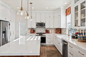 Kitchen with appliances with stainless steel finishes, a kitchen island, dark wood-style flooring, white cabinetry, and tasteful backsplash