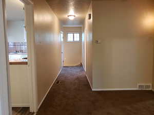 Hall featuring dark carpet and a textured ceiling