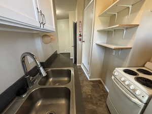 Kitchen featuring electric range, white cabinetry, open shelves, and dark stone finish floors