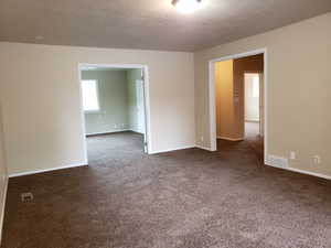 Empty room featuring dark carpet and a textured ceiling