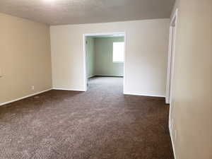 Empty room with dark colored carpet and a textured ceiling