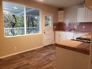 Kitchen featuring tile countertops, white cabinets, dark wood-style floors, decorative backsplash, and dishwasher