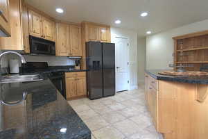 Kitchen with black appliances, recessed lighting, and light stone finish floors