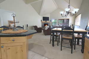 Dining area featuring a fireplace, high vaulted ceiling, light colored carpet, a chandelier, and beamed ceiling