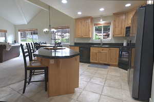 Kitchen with black appliances, light brown cabinets, dark countertops, a kitchen bar, and recessed lighting