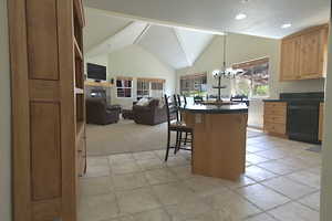 Kitchen featuring black dishwasher, dark countertops, a kitchen bar, a chandelier, and stone tile floors