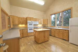 Kitchen featuring white appliances, high vaulted ceiling, light wood finished floors, tasteful backsplash, and light brown cabinets