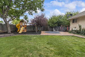 Fenced backyard featuring a trampoline and a playground