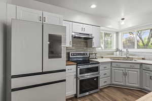 Kitchen with range with two ovens, white fridge, under cabinet range hood, decorative backsplash, and white cabinetry