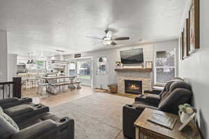 Living room with ceiling fan, a textured ceiling, wood finished floors, and a stone fireplace
