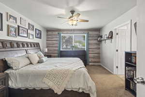 Bedroom featuring carpet, wood walls, an accent wall, and ceiling fan