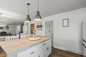Kitchen with wood counters, open floor plan, white cabinets, dark wood finished floors, and hanging light fixtures