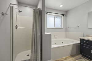 Bathroom featuring vanity, a jetted tub, a shower stall, and wood finished floors