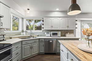Kitchen featuring stainless steel appliances, wood counters, gray cabinetry, decorative backsplash, and dark wood-style floors