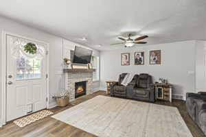 Living room with a ceiling fan, wood finished floors, and a stone fireplace