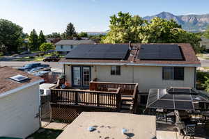 Rear view of house with a deck with mountain view, a shingled roof, solar panels, and outdoor dining area