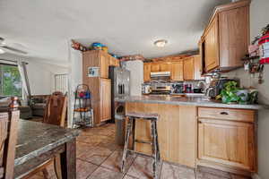 Kitchen with appliances with stainless steel finishes, under cabinet range hood, a peninsula, a textured ceiling, and light tile patterned flooring