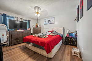 Bedroom with a textured ceiling, wood finished floors, and a ceiling fan