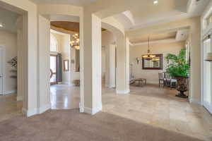 Foyer entrance with a chandelier, arched walkways, a tray ceiling, light tile patterned floors, and light colored carpet