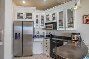 Kitchen featuring stainless steel refrigerator with ice dispenser, black dishwasher, dark countertops, white cabinetry, and glass insert cabinets