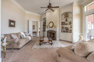Living area featuring light colored carpet, ornamental molding, a premium fireplace, built in features, and a ceiling fan